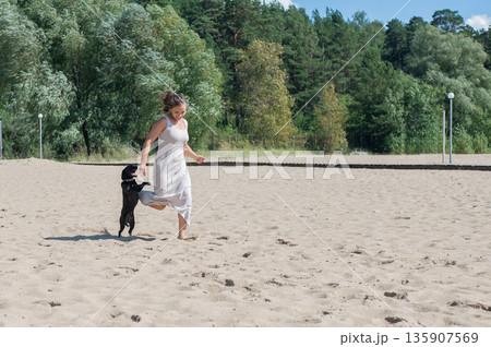 Caucasian woman walking on the beach with her dog.  135907569