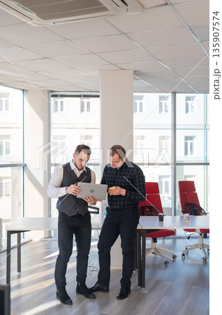 Two Caucasian men looking at a laptop and discussing work. Two Caucasian men looking at a laptop and discussing work. 135907574