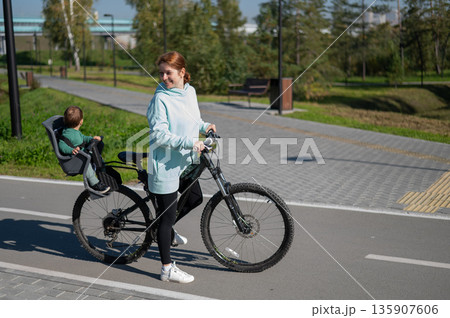 Caucasian woman rides bicycle with one-year-old son in park.  135907606