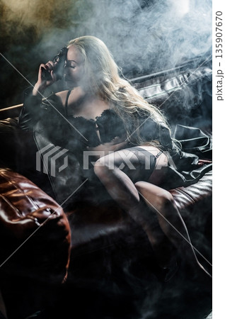 A Caucasian woman poses with a gun on a leather sofa. A Caucasian woman poses with a gun on a leather sofa. 135907670