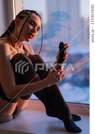 Caucasian woman holding a black dildo.  135907680