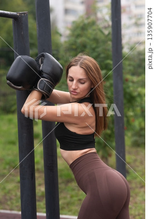 A Caucasian woman poses in boxing gloves on a sports field. 135907704