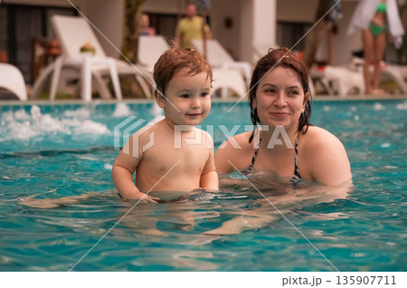 Caucasian woman holds her son while swimming in a pool on vacation. Mom teaches little boy to swim.  135907711