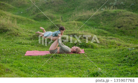 Caucasian woman doing yoga with her little son outdoors.  135907768