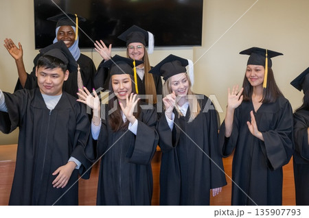 Young multinational people in graduation gowns stand at the lectern.  135907793