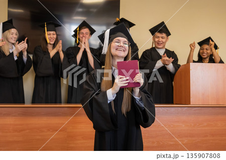 Happy Caucasian woman holds red diploma and classmates support her. Happy Caucasian woman holds red diploma and classmates support her. 135907808