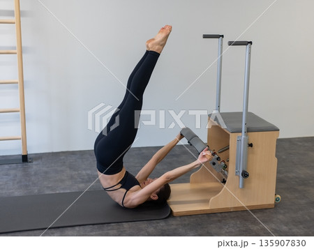 Caucasian woman doing Pilates on classic chair. Caucasian woman doing Pilates on classic chair. 135907830