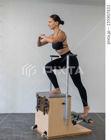 Caucasian woman doing Pilates on classic chair. Caucasian woman doing Pilates on classic chair. 135907831