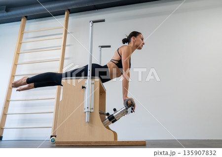 Caucasian woman doing Pilates on classic chair. Caucasian woman doing Pilates on classic chair. 135907832