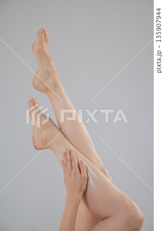 Woman applying moisturizer to her legs. White background.  135907944