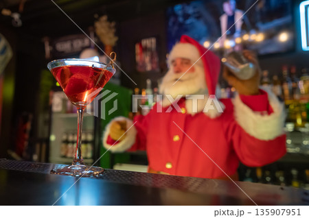 Santa Claus works at the bar making cocktails in a shaker.  135907951