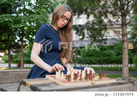 Caucasian woman playing chess outdoors. 135907974