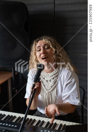 Caucasian woman singing into microphone and playing synthesizer and recording herself on laptop.  135907989