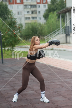 A Caucasian woman practices boxing outdoors.  135908056