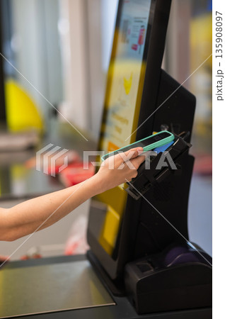 A woman pays using her smartphone at a self-checkout. A woman pays using her smartphone at a self-checkout. 135908097