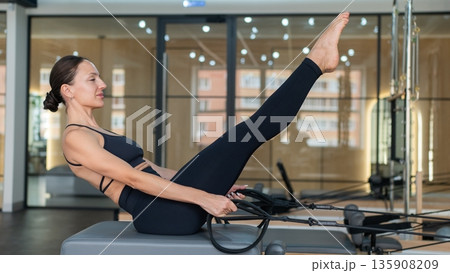 Caucasian woman doing exercises on reformer machine. Caucasian woman doing exercises on reformer machine. 135908209