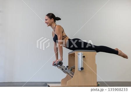 Caucasian woman doing Pilates on classic chair. Caucasian woman doing Pilates on classic chair. 135908233