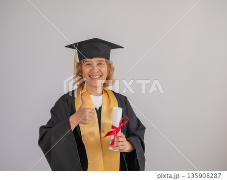 Happy senior woman in graduation gown holding diploma on white background. Happy senior woman in graduation gown holding diploma on white background. 135908287
