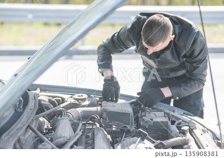 A man changes spark plugs in his car. A man changes spark plugs in his car. 135908381