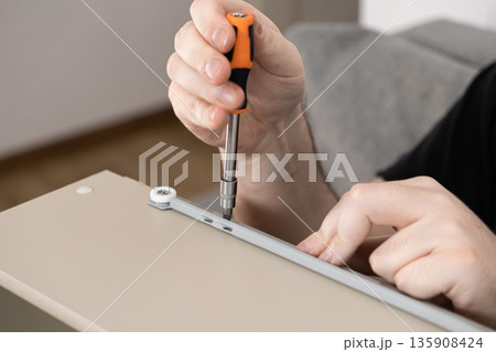 Man's hands carefully using a screwdriver to install a drawer runner on furniture, representing home improvement, assembly, and DIY projects 135908424