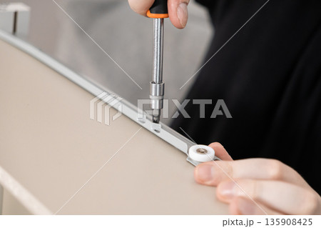 A person's hands precisely assemble modern furniture, using a screwdriver to attach a sliding drawer mechanism, symbolizing practical home improvement and DIY skill A person's hands precisely assemble modern furniture, using a screwdriver to attach a sliding drawer mechanism, symbolizing practical home improvement and DIY skill 135908425
