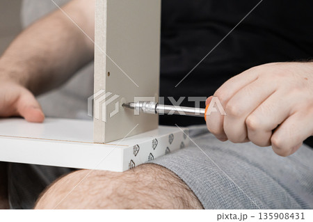 Person's hands meticulously using a screwdriver to assemble a light-colored furniture piece, symbolizing practical DIY home improvement and focused manual work 135908431