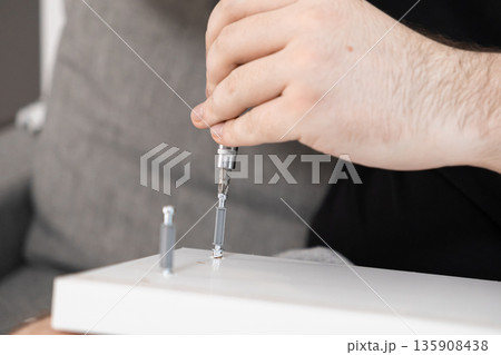 Male hand utilizing a screwdriver to assemble white flat-pack furniture, symbolizing home improvement, practical repair, and do-it-yourself project completion 135908438