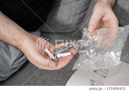 Person's hands organizing small furniture assembly hardware, including screws and wall plugs, with an instruction manual, for home DIY project Person's hands organizing small furniture assembly hardware, including screws and wall plugs, with an instruction manual, for home DIY project 135908452