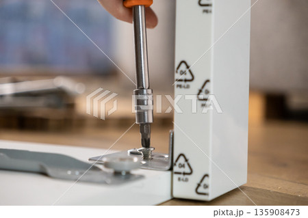 Hand using a screwdriver to assemble white furniture panel with a metal bracket, highlighting DIY home improvement and the importance of PE-LD plastic recycling 135908473