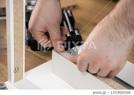 Dedicated hands carefully assembling a piece of modern white flat-pack furniture, showcasing a rewarding DIY home improvement project and efficient self-assembly Dedicated hands carefully assembling a piece of modern white flat-pack furniture, showcasing a rewarding DIY home improvement project and efficient self-assembly 135908506
