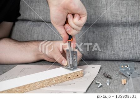 Adult's hands diligently assembling flat-pack furniture using a screwdriver, carefully following instructions for a home improvement project, symbolizing personal effort, practical skills 135908533