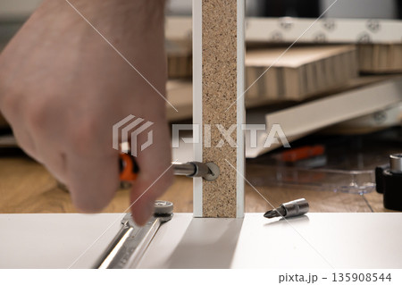 Person's hand assembling new furniture, tightening a screw into a white particle board panel, showcasing home improvement and successful DIY craftsmanship 135908544