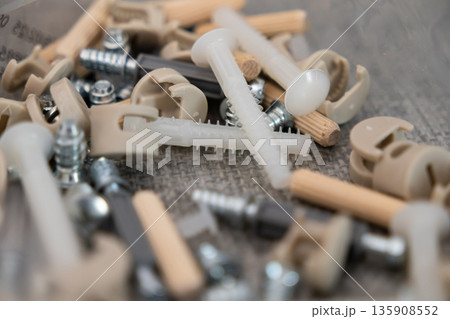 Detailed close-up of various furniture assembly hardware, showcasing screws, wooden dowels, plastic pins, and cam lock connectors for DIY home construction Detailed close-up of various furniture assembly hardware, showcasing screws, wooden dowels, plastic pins, and cam lock connectors for DIY home construction 135908552