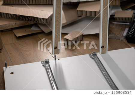 Assembly of white particle board furniture with a screw connection on a wooden floor, representing home improvement, DIY project, and flat-pack furniture construction process Assembly of white particle board furniture with a screw connection on a wooden floor, representing home improvement, DIY project, and flat-pack furniture construction process 135908554