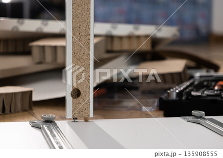 DIY furniture assembly in progress, showcasing a particle board panel joining another piece with a cam lock and dowel, representing modern home furnishing 135908555