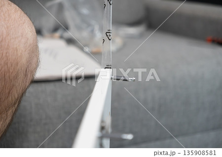 White furniture panel being assembled with a metallic dowel and screw connector, highlighting DIY home improvement in a domestic setting White furniture panel being assembled with a metallic dowel and screw connector, highlighting DIY home improvement in a domestic setting 135908581