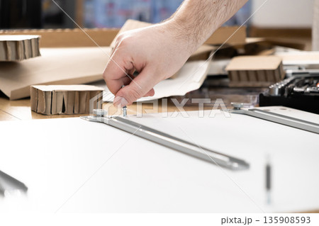 A person's hand carefully screws a metal bolt into a white furniture panel, illustrating the process of DIY assembly for home improvement projects 135908593