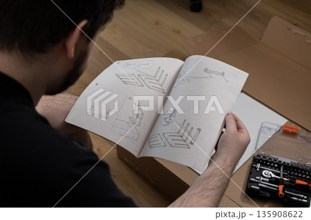 Young adult carefully reading detailed furniture assembly guide for a new purchase, focused on successful DIY home improvement project setup 135908622
