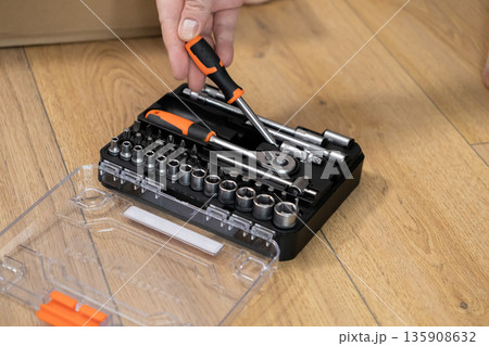 Hand selecting an orange and black screwdriver from a comprehensive mechanic tool kit, perfectly organized for versatile home improvement and essential DIY tasks 135908632