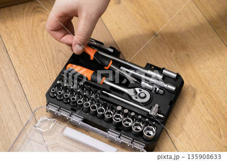 Hand opening an organized tool kit with screwdriver bits, sockets, and a ratchet, essential for versatile home repairs and DIY 135908633