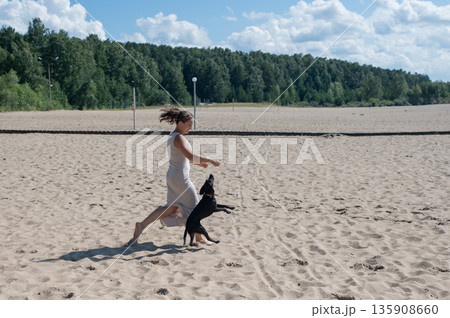 Caucasian woman walking on the beach with her dog.  135908660