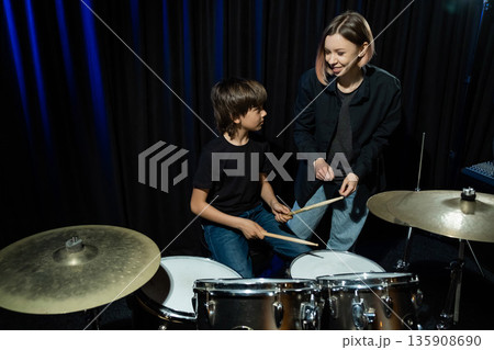 Young caucasian woman teaches a boy to play the drums in the studio on a black background. Music school student Young caucasian woman teaches a boy to play the drums in the studio on a black background. Music school student 135908690