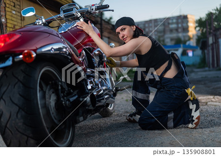 Brunette woman repairs a red motorcycle. Brunette woman repairs a red motorcycle. 135908801