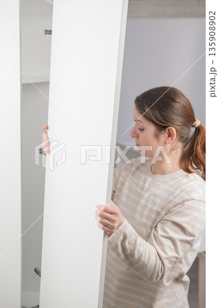 A Caucasian woman assembles a wardrobe. A Caucasian woman assembles a wardrobe. 135908902