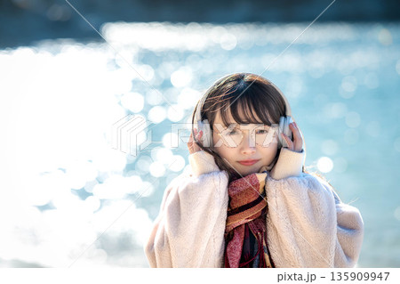 冬の海でヘッドホンで音楽を聴く若い女性 135909947