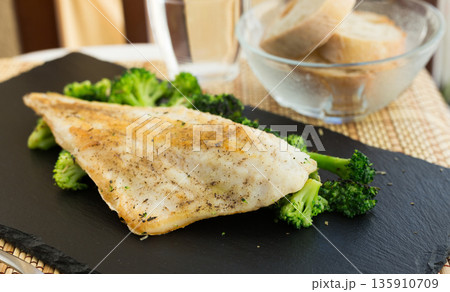 fried fillet of sea bass with garnish of broccoli on black warm stone plate 135910709