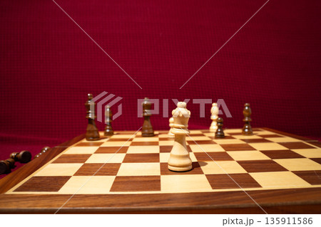 White king piece on a wooden chessboard with other pieces blurred in the background. Close-up view of a game in progress. Concept of strategy, chess, focus, board game, intellectual activity. White king piece on a wooden chessboard with other pieces blurred in the background. Close-up view of a game in progress. Concept of strategy, chess, focus, board game, intellectual activity. 135911586