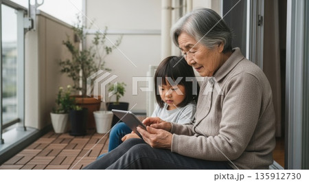 ベランダで孫と一緒にタブレットを楽しむ祖母 135912730