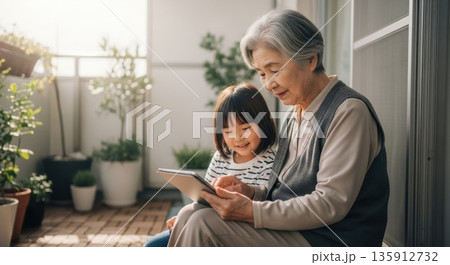 ベランダで孫と一緒にタブレットを楽しむ祖母 135912732