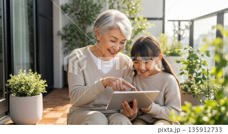 ベランダで孫と一緒にタブレットを楽しむ祖母 135912733